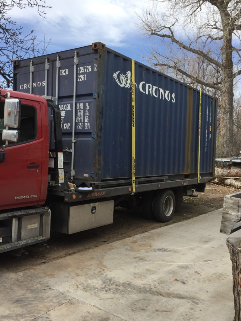 A 20-foot shipping container on a tilt-bed delivery truck